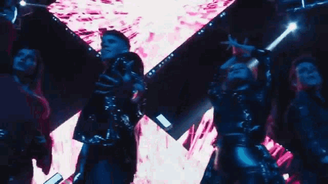 a group of people are dancing in front of a large screen in a dark room .