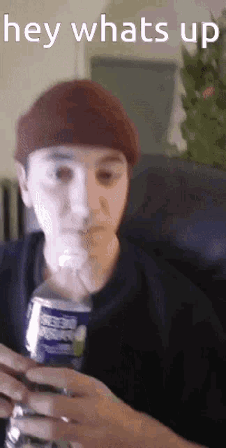 a man in a beanie is holding a can of soda and a bottle of water with the words hey whats up above him