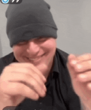 a man wearing a black beanie and a black shirt is smiling and making a funny face .
