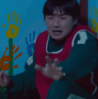 a man in a red and green vest with the number 12 on it is standing in front of a wall with handprints on it .