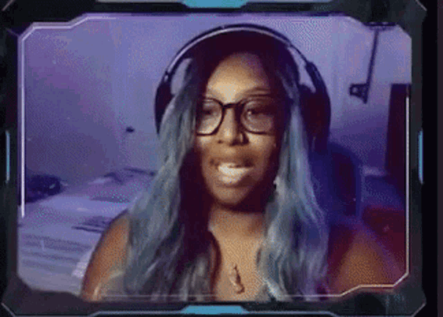 a woman with blue hair and glasses is wearing headphones and smiling at the camera .