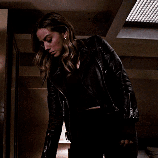a woman in a leather jacket is holding an envelope in her hand
