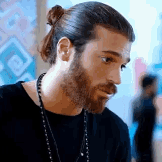 a man with long hair and a beard is wearing a ponytail and a necklace .