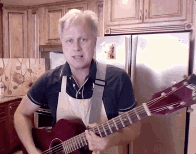 a man in an apron is playing a red guitar in front of a refrigerator
