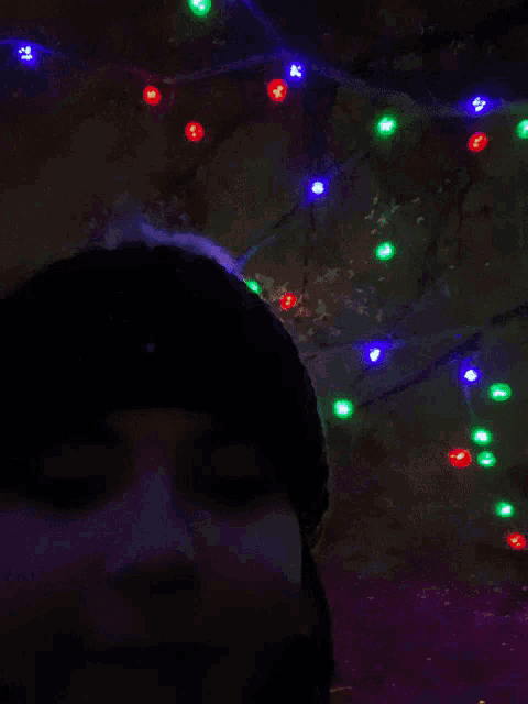 a woman wearing a green knitted hat stands in front of christmas lights