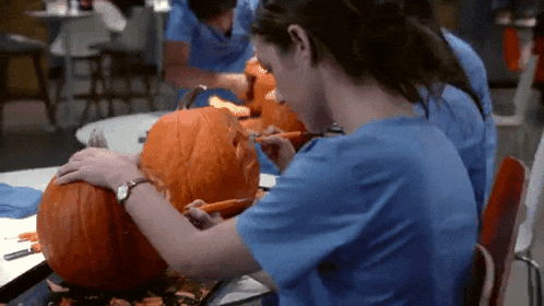 a woman in scrubs is carving a pumpkin with a knife
