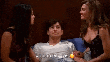 two women are touching a man 's stomach while sitting on a bed .