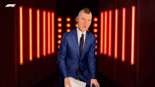 a man in a blue suit and tie holds a piece of paper in front of a sign that says f1
