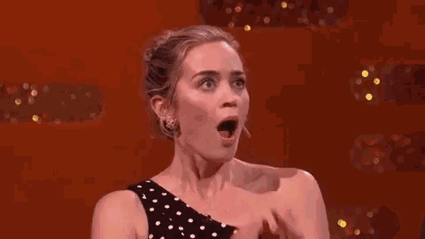 a woman in a polka dot dress is covering her mouth with her hands and making a surprised face .