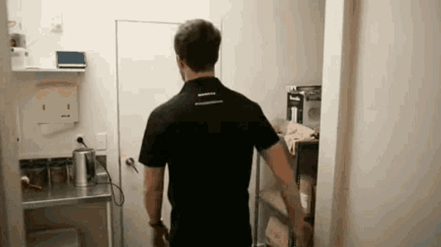 a man in a black shirt is standing in a room with a shelf .