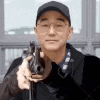 a man wearing glasses and a hat is holding a gun in his hand .