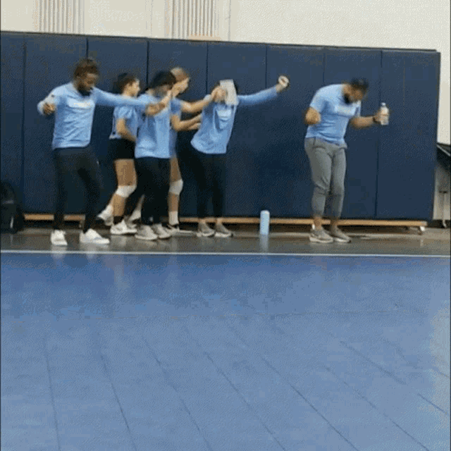 a group of people are standing on a blue floor in a gym .