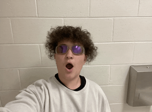 a young man wearing sunglasses and a white sweater takes a selfie