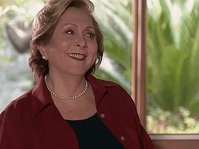 a woman wearing a pearl necklace and a red shirt smiles