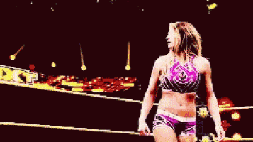 a woman in a purple top and purple shorts is walking in a wrestling ring .