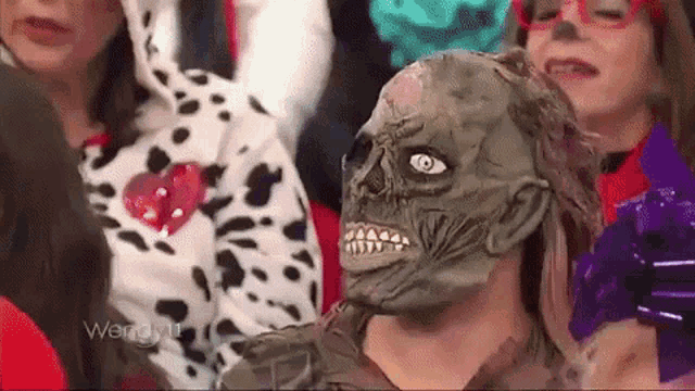 a woman wearing a zombie mask is sitting in front of a group of people .