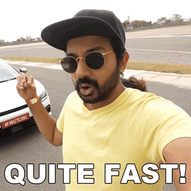 a man wearing sunglasses and a hat says " quite fast " in front of a car