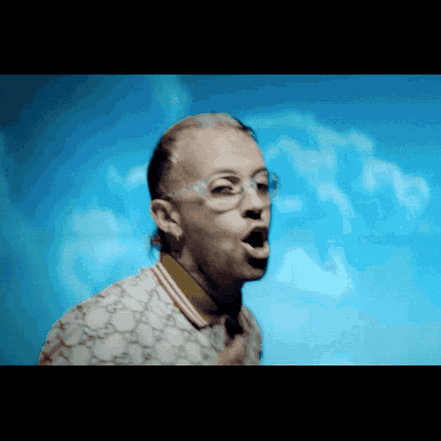 a man wearing glasses and a gucci shirt is singing into a microphone