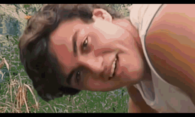 a man in a white tank top is smiling and looking at the camera