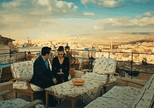 a man and a woman sit on a patio with a view of a city