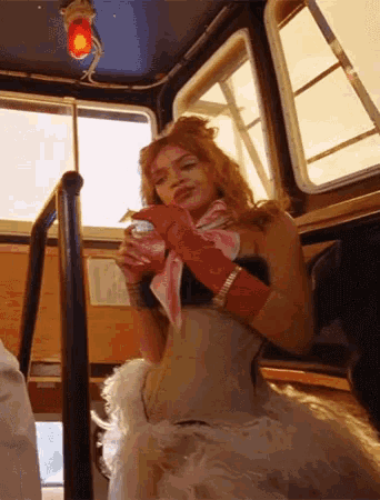 a woman wearing a corset and red gloves is sitting on a bus