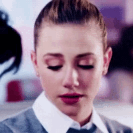 a close up of a woman 's face with her eyes closed . she is wearing a white shirt and tie .