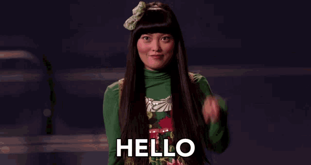 a woman with long black hair is waving her hand and says hello