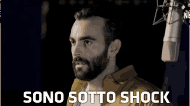 a man with a beard is standing in front of a microphone and the words sono sotto shock are written below him