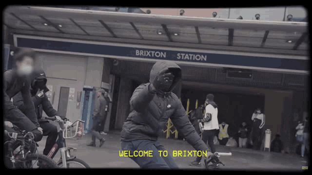 a group of people riding bicycles in front of a sign that says brixton station