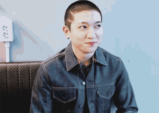 a man with a shaved head wears a denim jacket and earrings