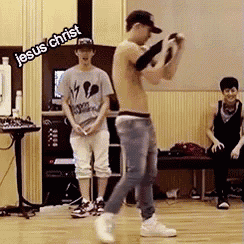 a shirtless man is dancing in a room with jesus christ written on the wall above him