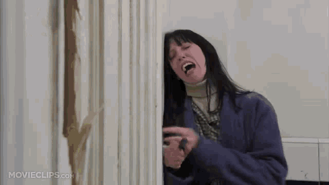 a woman in a purple coat is screaming while holding a knife behind a door .