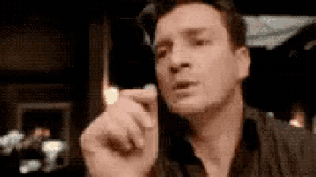 a man is talking on a cell phone while sitting at a table in a dark room .