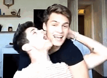 two young men are playing with each other in a living room and one is holding the other 's neck .