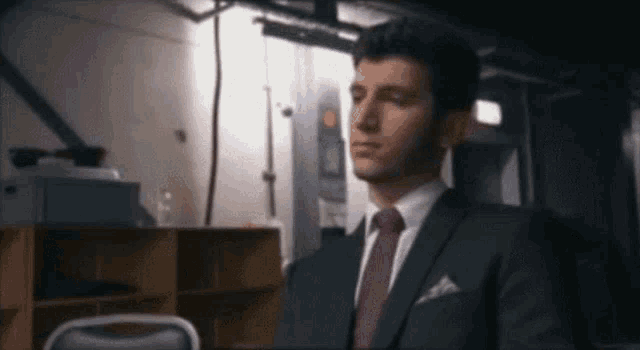 a man in a suit and tie is sitting in a dark room