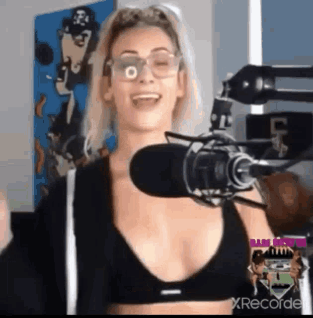a woman is talking into a microphone while wearing glasses and a black bra .
