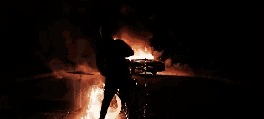 a man playing drums in front of a drum set on fire .