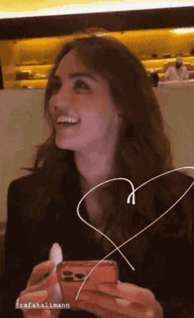 a woman is smiling while holding a cell phone with rafakalimann written on the bottom