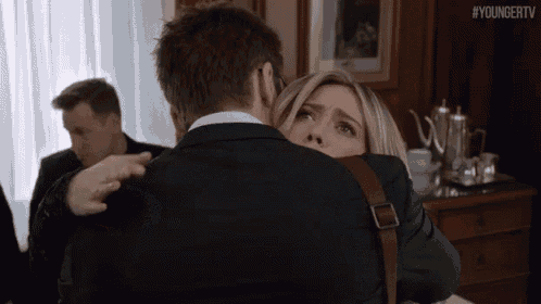 a man in a suit is hugging a woman in a room with #youngertv written on the bottom of the image .