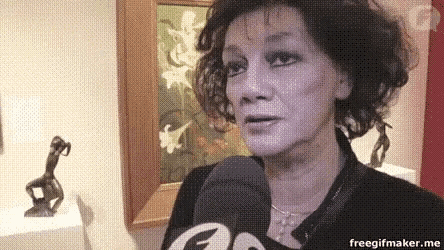 a woman is talking into a microphone in front of a painting and statue .