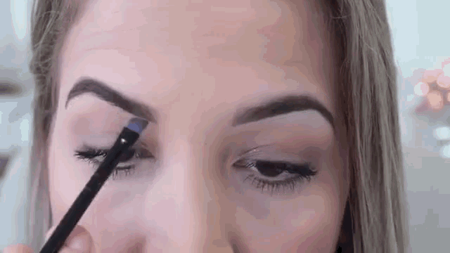 a close up of a woman applying eyebrow pencil to her eyebrows .