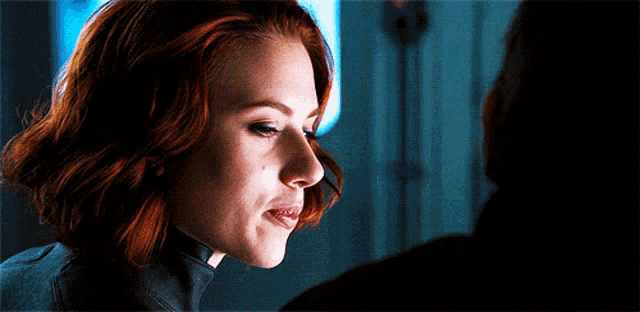 a close up of a woman with red hair looking at a man in a dark room .