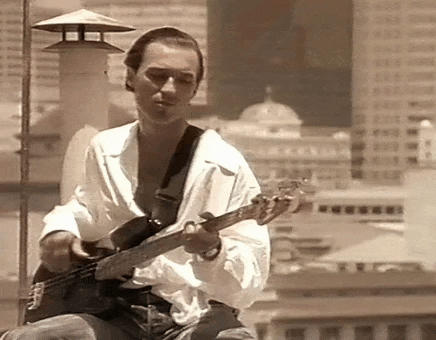 a man is playing a bass guitar on a rooftop in front of a city .