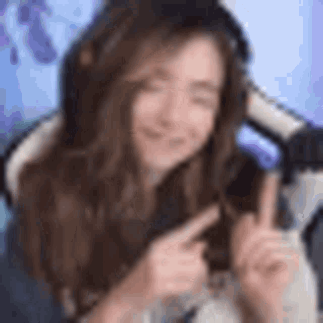 a woman is sitting in a chair wearing headphones and pointing at the camera .