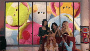 a group of girls are sitting on a couch in front of a window with stuffed animals in the background