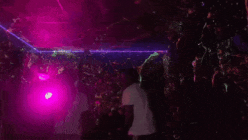a man in a white t-shirt is dancing in a dark room with purple lights