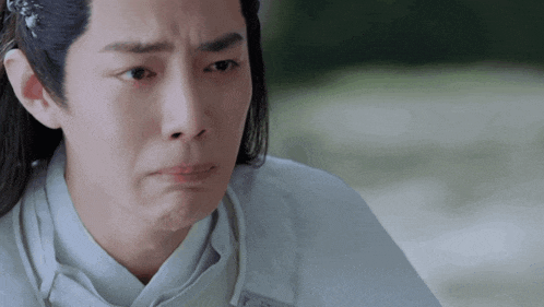a man with long hair and a white shirt is making a sad face