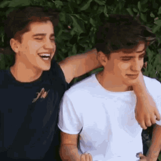 two boys are laughing and hugging each other while sitting next to each other .