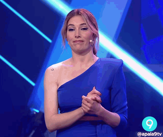 a woman in a blue dress stands in front of a microphone with the number 9 behind her