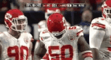 a group of football players are standing on a field and one of them is wearing a helmet with the number 50 on it .